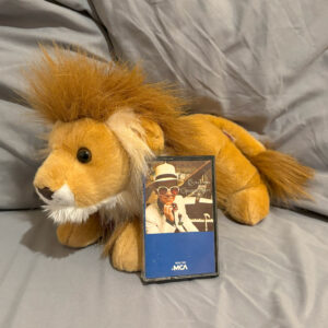 small lion stuffed animal with Elton John's Greatest Hits cassette tape